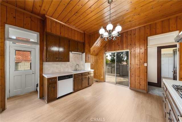 kitchen featuring pendant lighting, sink, dishwasher, wooden walls, and dark brown cabinetry