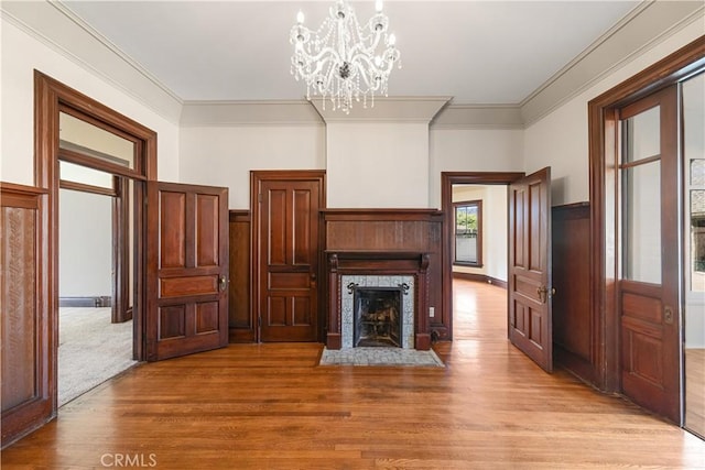 unfurnished living room with crown molding, a chandelier, and light wood-type flooring