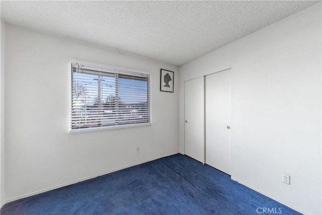 unfurnished bedroom with a closet, a textured ceiling, and dark colored carpet