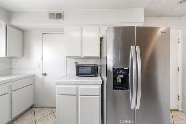 kitchen with white cabinetry, stainless steel fridge with ice dispenser, light tile patterned floors, and tile countertops