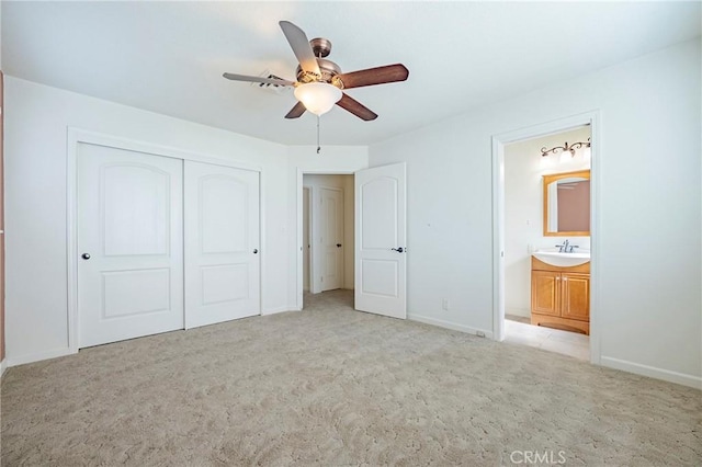 unfurnished bedroom featuring connected bathroom, sink, light carpet, a closet, and ceiling fan