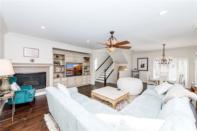 living room featuring dark wood-type flooring, crown molding, a tiled fireplace, and ceiling fan with notable chandelier