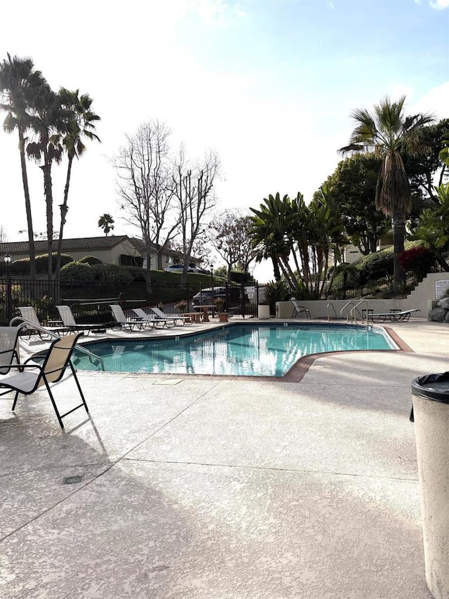 community pool with a patio area and fence