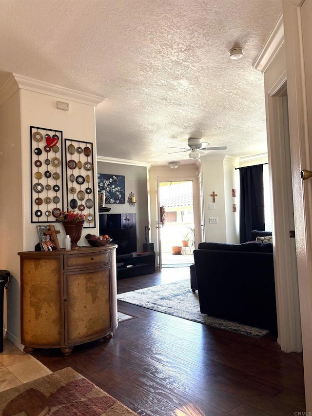 living room with a ceiling fan, a textured ceiling, ornamental molding, and dark wood-type flooring