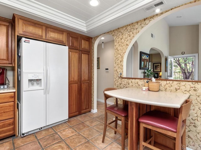 kitchen featuring crown molding, a tray ceiling, white fridge with ice dispenser, a kitchen bar, and kitchen peninsula