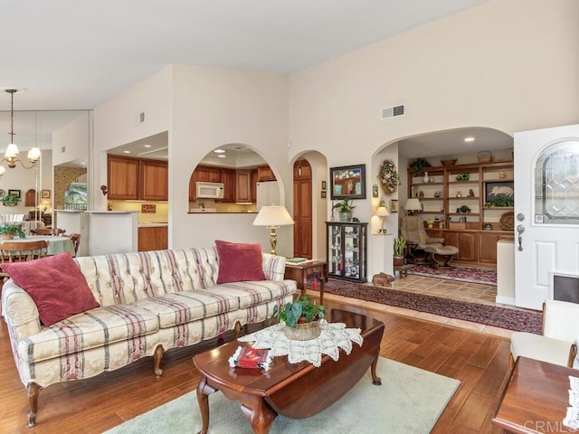 living room with an inviting chandelier, a towering ceiling, light hardwood / wood-style floors, and built in features