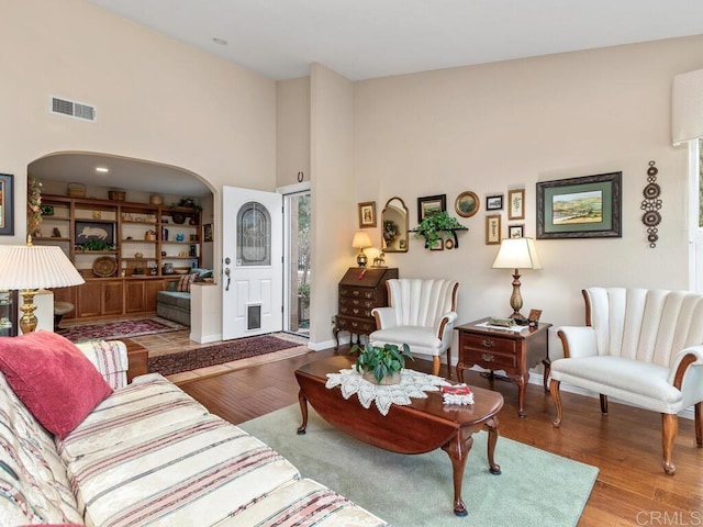 living room with built in shelves, a towering ceiling, and light hardwood / wood-style floors