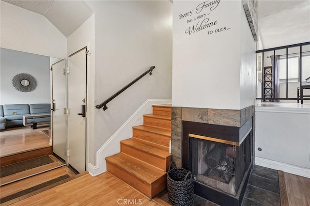 stairway with a tile fireplace, vaulted ceiling, and hardwood / wood-style floors