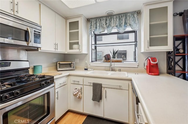 kitchen featuring stainless steel appliances, white cabinetry, sink, and light hardwood / wood-style flooring