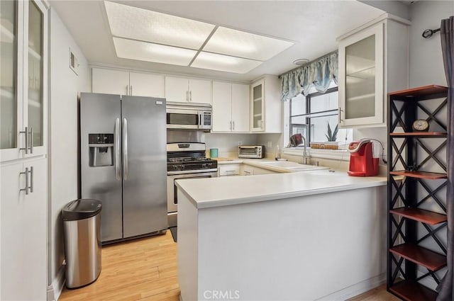 kitchen featuring appliances with stainless steel finishes, white cabinetry, sink, light hardwood / wood-style floors, and kitchen peninsula