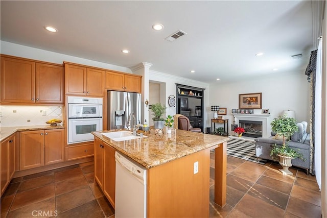 kitchen with sink, white appliances, light stone countertops, a kitchen island with sink, and backsplash