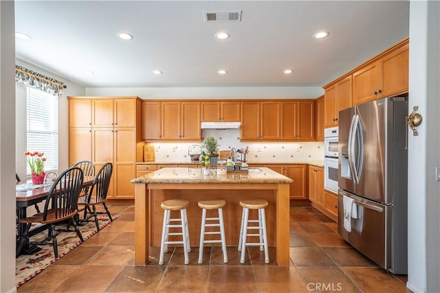 kitchen with white double oven, stainless steel fridge, a kitchen breakfast bar, a kitchen island, and backsplash