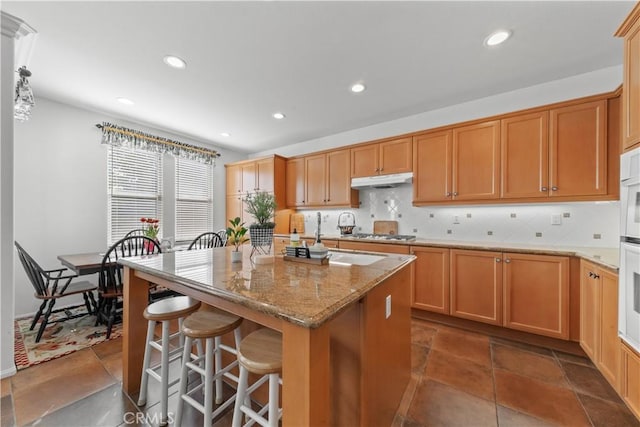 kitchen featuring stainless steel gas cooktop, tasteful backsplash, light stone counters, a center island, and hanging light fixtures