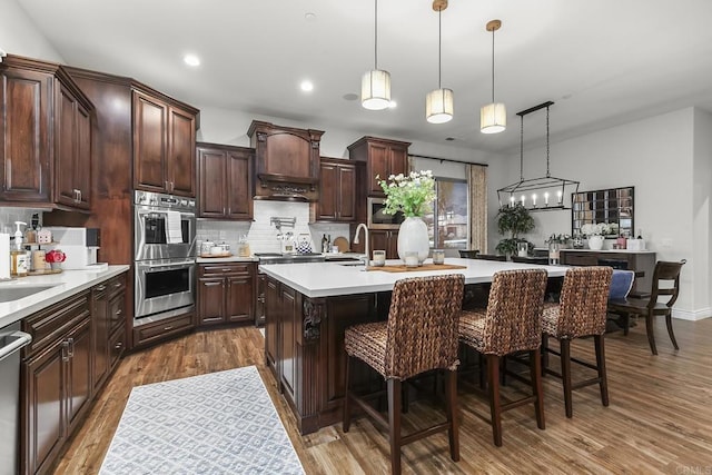 kitchen with dark brown cabinetry, a breakfast bar, decorative light fixtures, stainless steel appliances, and a kitchen island with sink