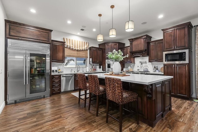 kitchen featuring pendant lighting, dark wood-type flooring, a center island, built in appliances, and a kitchen bar