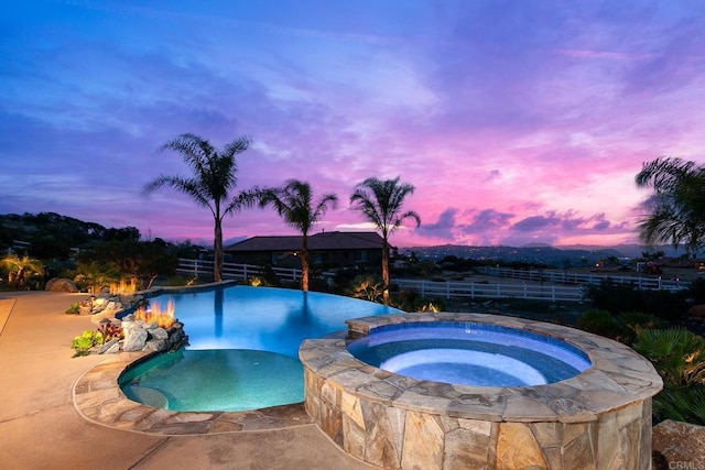 pool at dusk featuring an in ground hot tub and a patio area