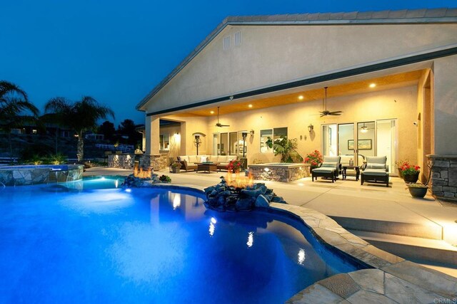 pool at night featuring an in ground hot tub, an outdoor living space with a fire pit, ceiling fan, and a patio