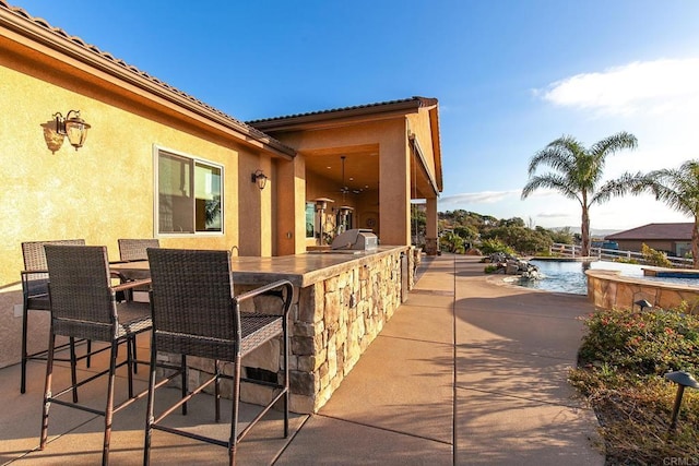 view of patio / terrace featuring a bar, a water view, ceiling fan, and an outdoor kitchen