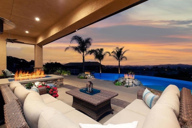 patio terrace at dusk featuring a water view, an outdoor living space with a fire pit, and ceiling fan