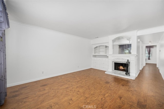 unfurnished living room with a warm lit fireplace, wood finished floors, and ornamental molding