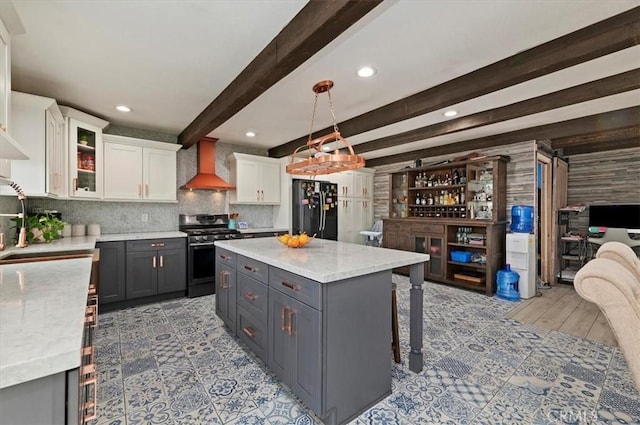 kitchen featuring gray cabinetry, stainless steel gas range oven, white cabinets, black fridge, and wall chimney exhaust hood