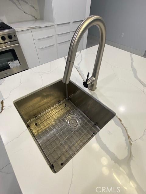 7631 Columbia St, Rosemead, CA 91770 - kitchen view of a sink, gas range, white cabinetry, and light stone counters