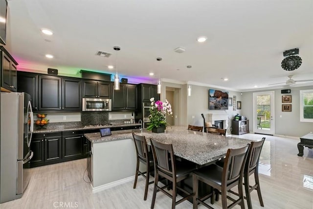 kitchen with a kitchen bar, light stone counters, decorative light fixtures, appliances with stainless steel finishes, and an island with sink