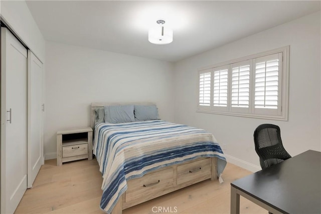 bedroom with light wood finished floors, a closet, and baseboards