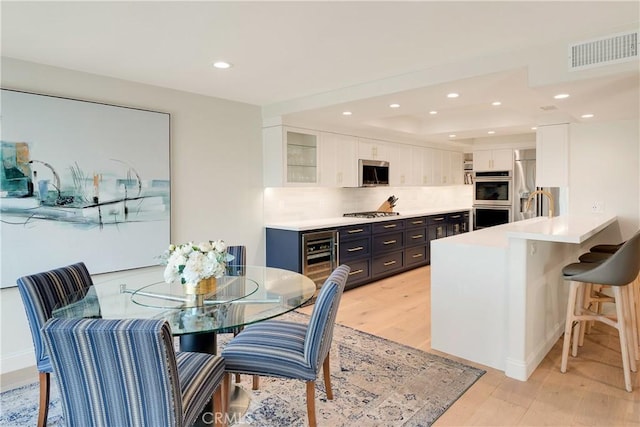 kitchen featuring stainless steel appliances, light wood-style floors, a kitchen bar, visible vents, and white cabinets