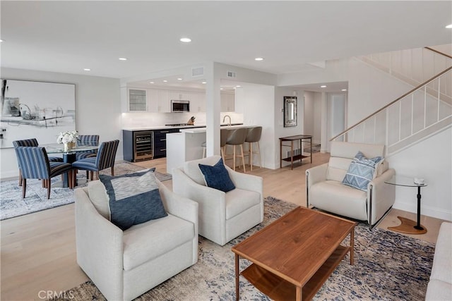 living area featuring recessed lighting, light wood-type flooring, stairs, visible vents, and beverage cooler