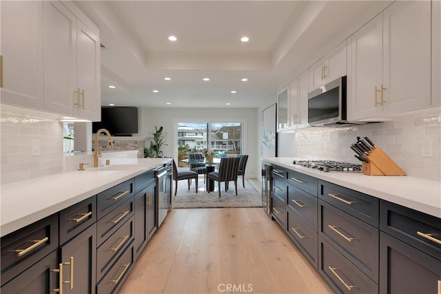 kitchen featuring white cabinets, light wood-style floors, appliances with stainless steel finishes, and a tray ceiling