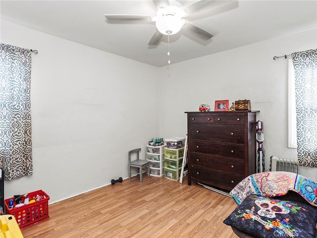 bedroom with ceiling fan, radiator heating unit, and light wood-type flooring