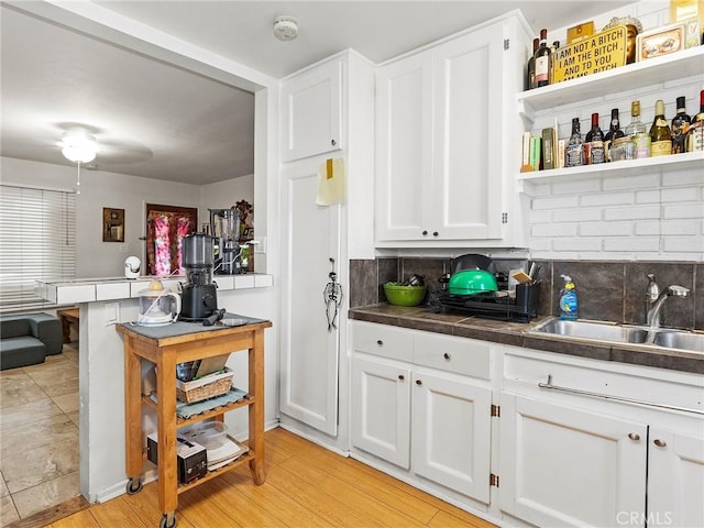 bar with tasteful backsplash, white cabinetry, sink, and light hardwood / wood-style floors