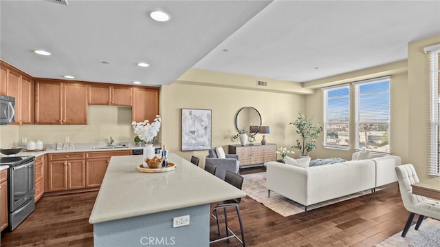 kitchen with dark wood-type flooring, stainless steel appliances, a breakfast bar, a center island, and sink