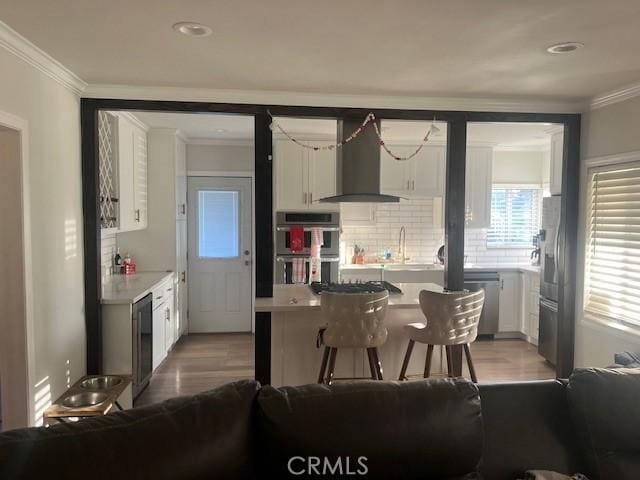 kitchen featuring white cabinetry, crown molding, appliances with stainless steel finishes, decorative backsplash, and wall chimney range hood