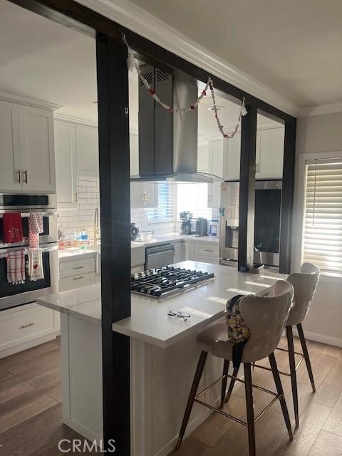 kitchen with a breakfast bar, white cabinetry, crown molding, light wood-type flooring, and appliances with stainless steel finishes