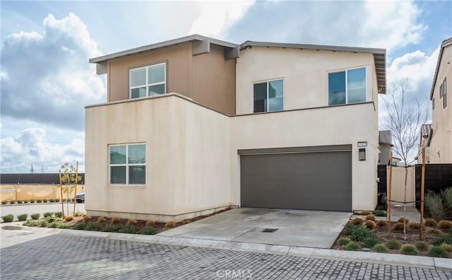 view of front of home with decorative driveway, an attached garage, fence, and stucco siding