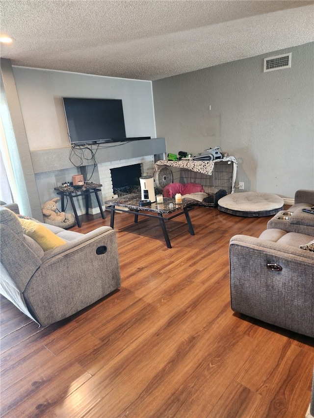 living room featuring hardwood / wood-style floors, a textured ceiling, and a brick fireplace