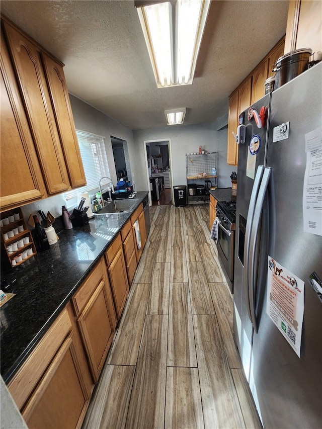 kitchen with dark stone countertops, sink, stainless steel appliances, and a textured ceiling