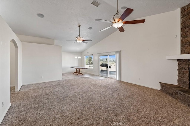 unfurnished living room featuring high vaulted ceiling, a stone fireplace, ceiling fan with notable chandelier, and light colored carpet