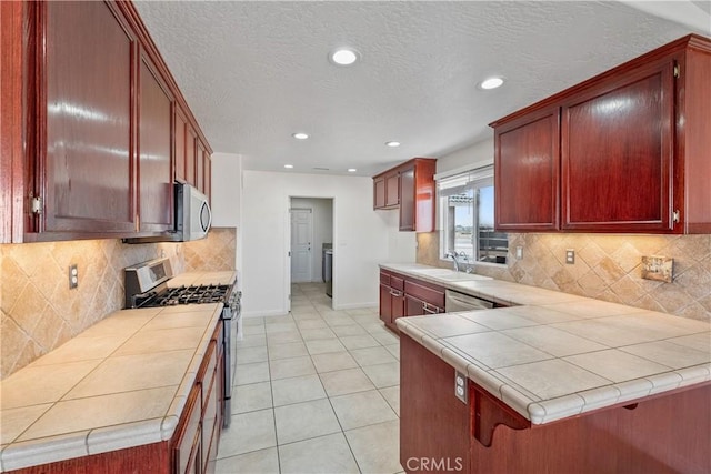 kitchen featuring sink, appliances with stainless steel finishes, tile counters, light tile patterned flooring, and kitchen peninsula