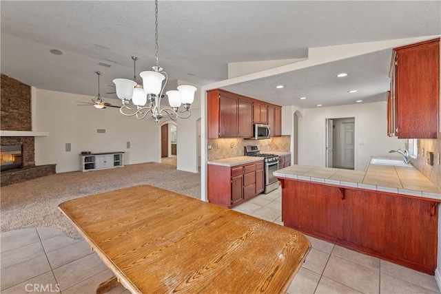 kitchen with tile countertops, hanging light fixtures, kitchen peninsula, stainless steel appliances, and a fireplace