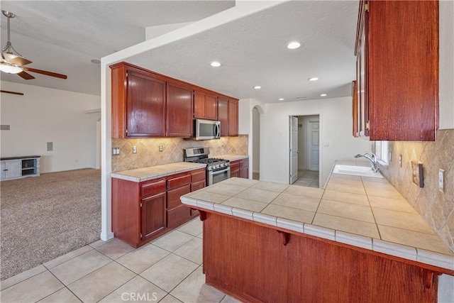 kitchen featuring sink, ceiling fan, stainless steel appliances, tile counters, and light colored carpet