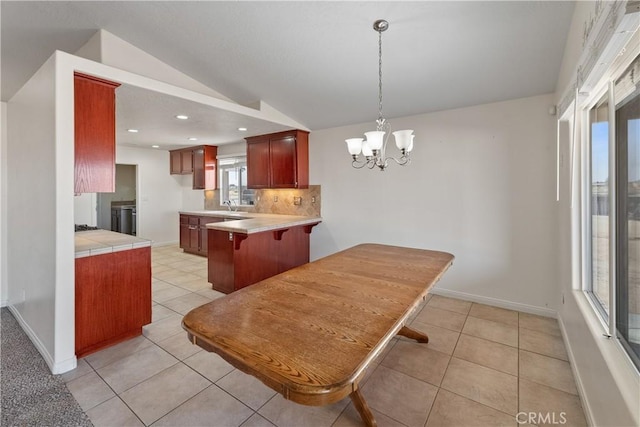 kitchen with lofted ceiling, sink, light tile patterned floors, backsplash, and kitchen peninsula