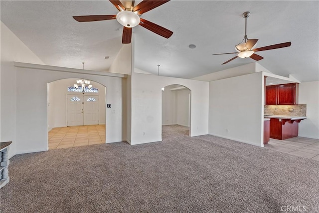 unfurnished living room with ceiling fan with notable chandelier, vaulted ceiling, and light colored carpet