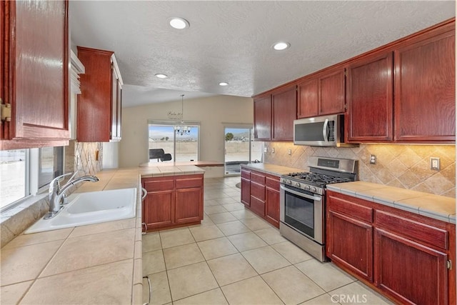 kitchen with sink, appliances with stainless steel finishes, tile counters, decorative light fixtures, and vaulted ceiling