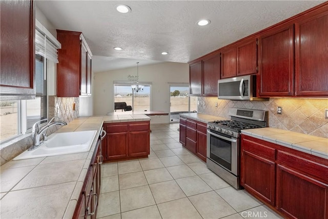 kitchen with sink, vaulted ceiling, hanging light fixtures, appliances with stainless steel finishes, and tile counters