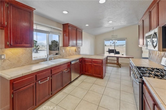 kitchen featuring stainless steel appliances, tile counters, kitchen peninsula, and sink