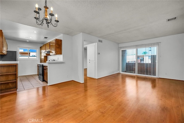 unfurnished living room with an inviting chandelier, a textured ceiling, and light wood-type flooring