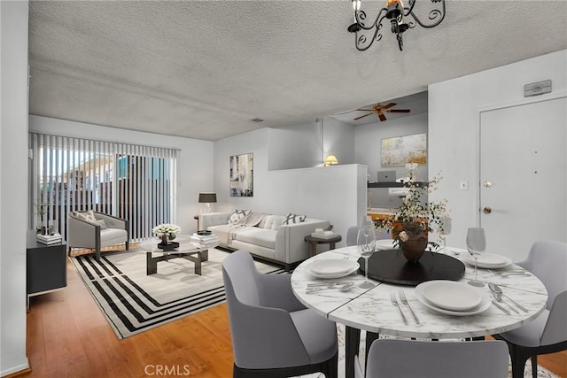 dining space with hardwood / wood-style flooring, ceiling fan with notable chandelier, and a textured ceiling